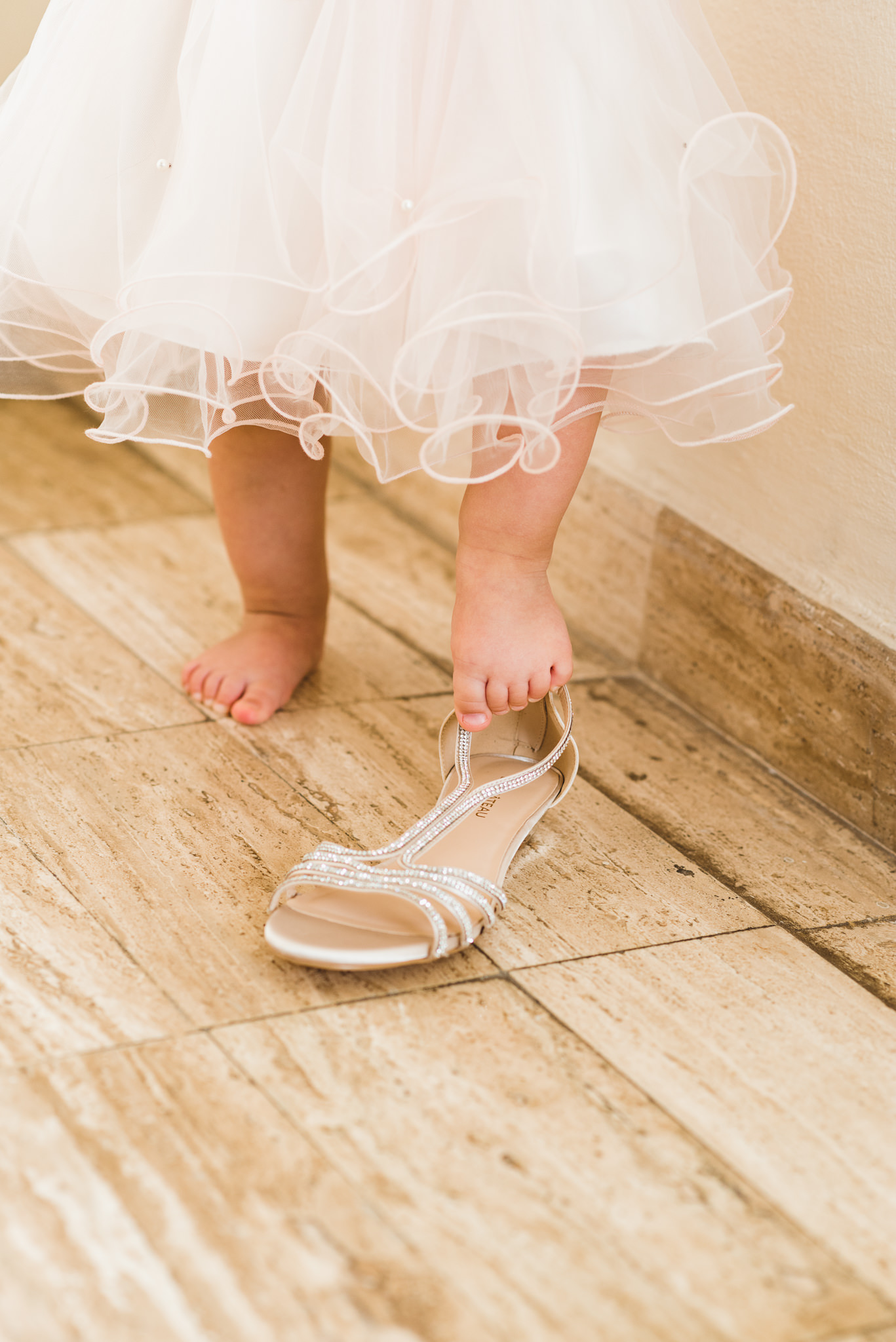 baby in a dress trying to get her foot into brides wedding shoe before ceremony at Now Sapphire Resort in Mexico