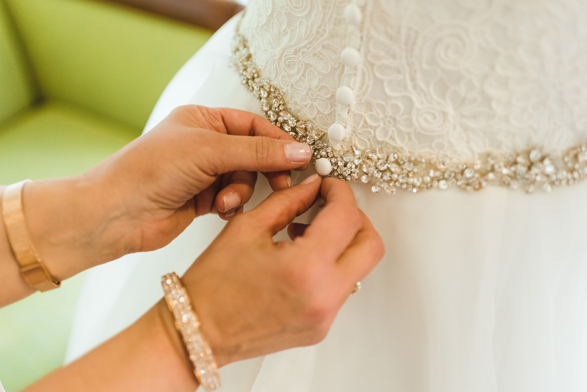 woman doing up buttons of brides white wedding dress covered with jewels ahead of ceremony at Now Sapphire Resort in Mexico