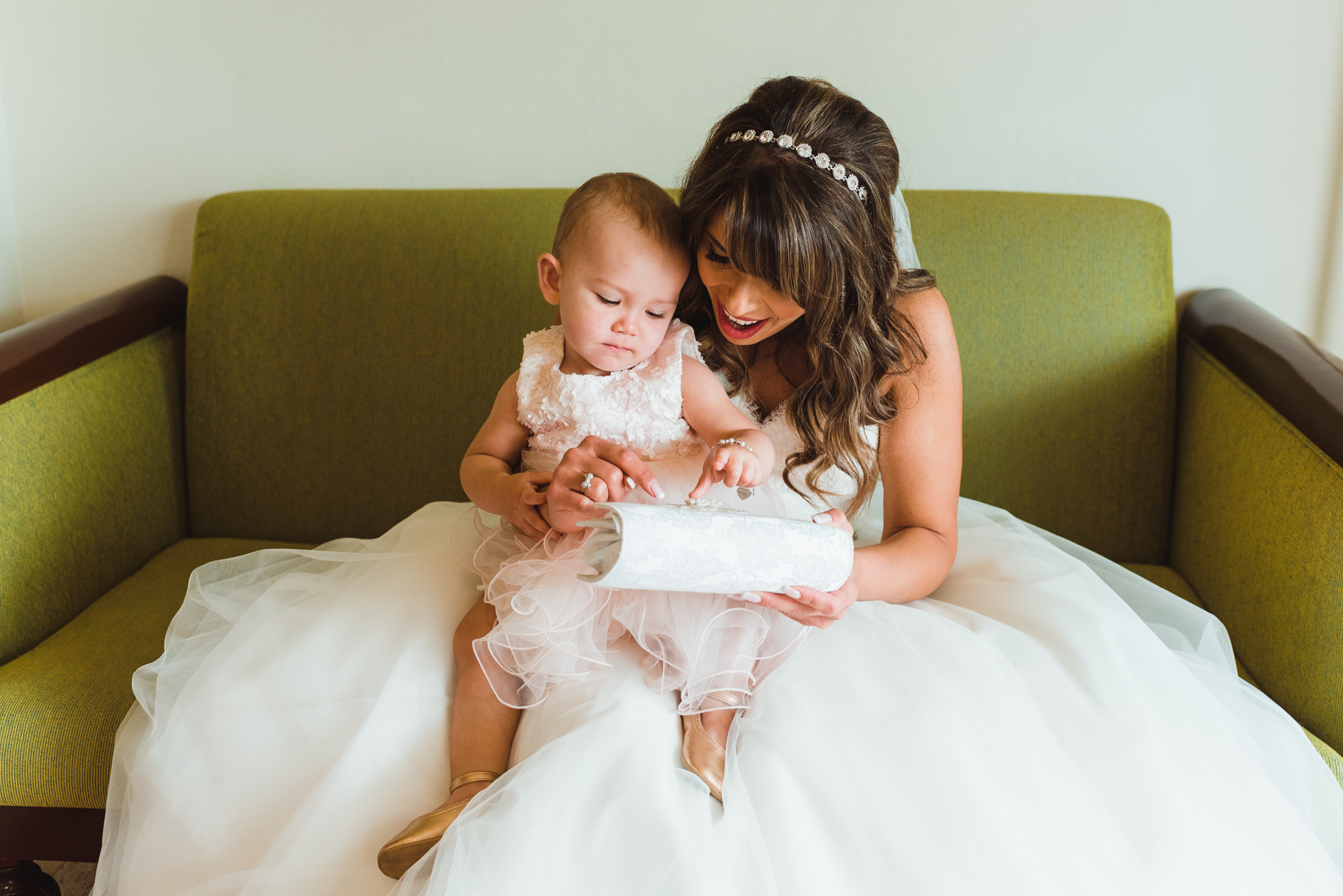 bride sitting in a green chair in her white wedding dress with a baby showing her her white purse before wedding ceremony at Now Sapphire Resort in Mexico