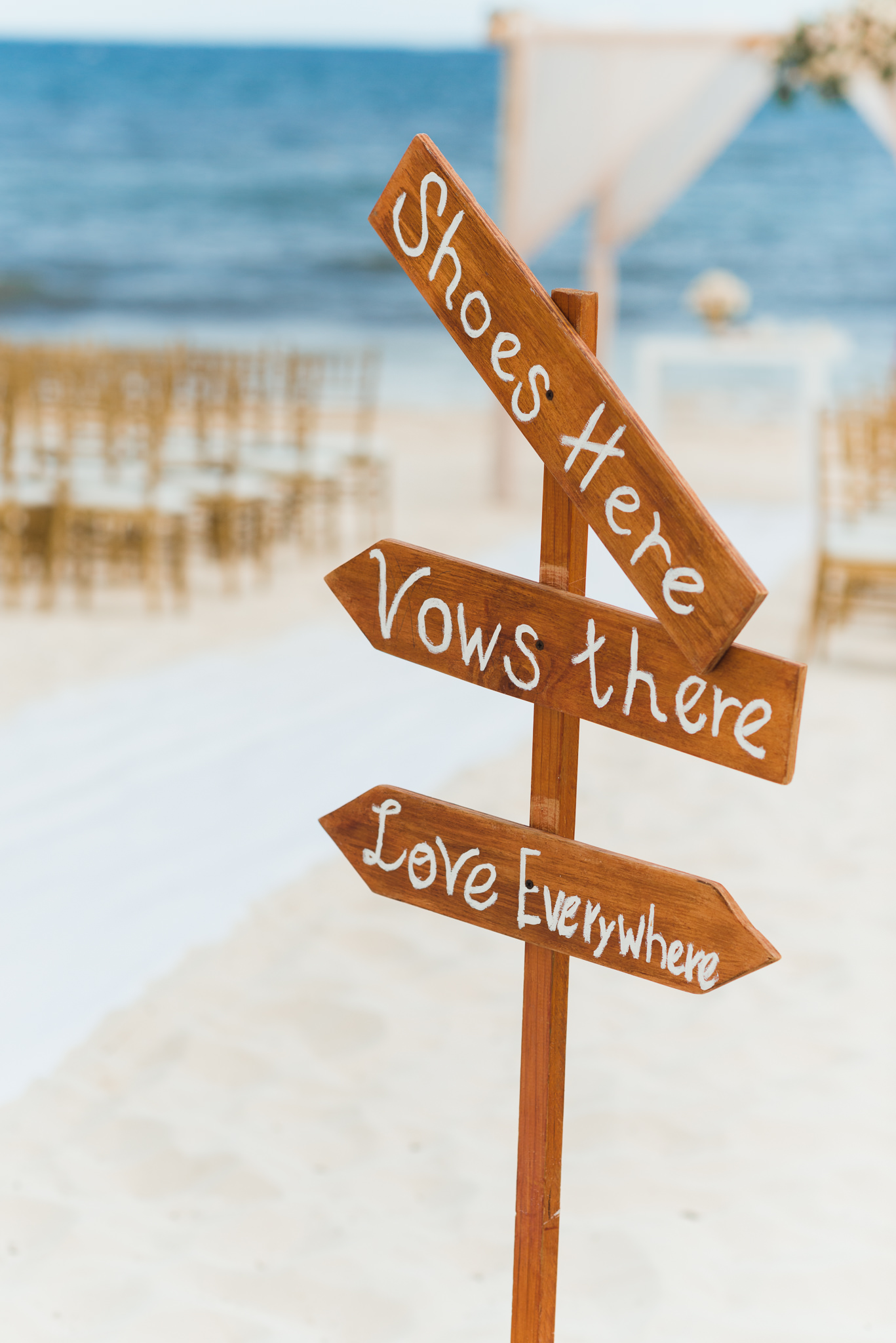 sign with arrows reading "shoes here, vows there, love everywhere" at the entrance of beach destination wedding at Now Sapphire Resort in Mexico