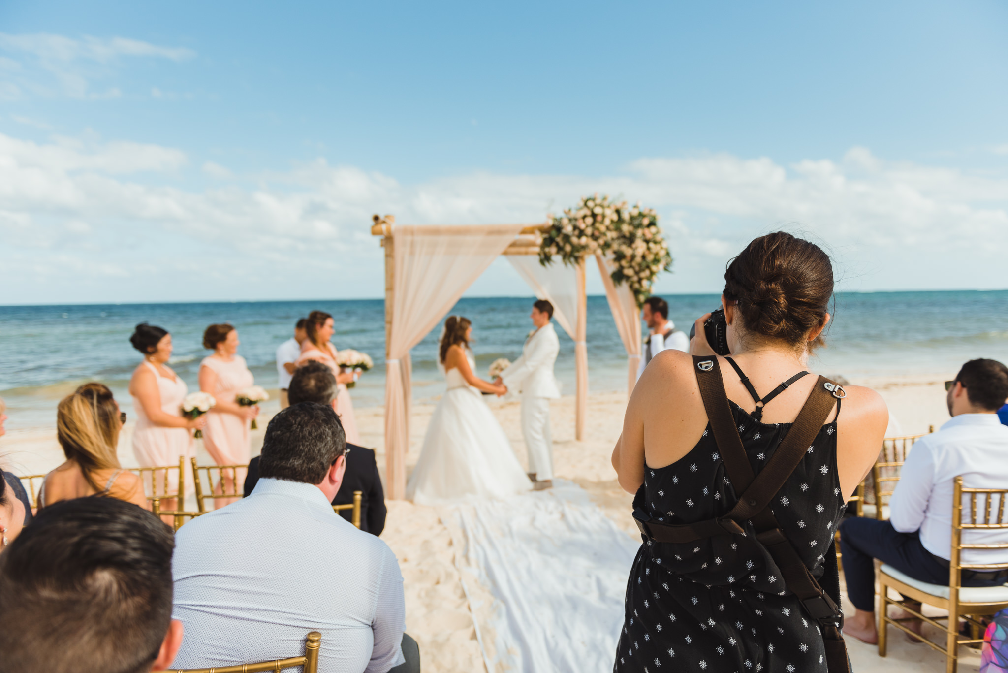 photography taking picture of brides holding hands during beach ceremony in front of ocean at Now Sapphire Resort in Mexico