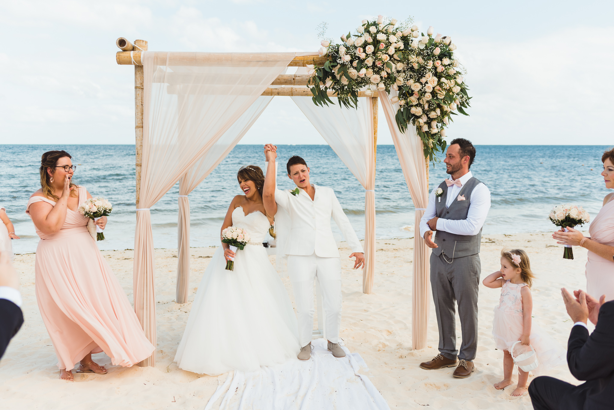 brides lifting hands together after beach ceremony in front of ocean at Now Sapphire Resort in Mexico