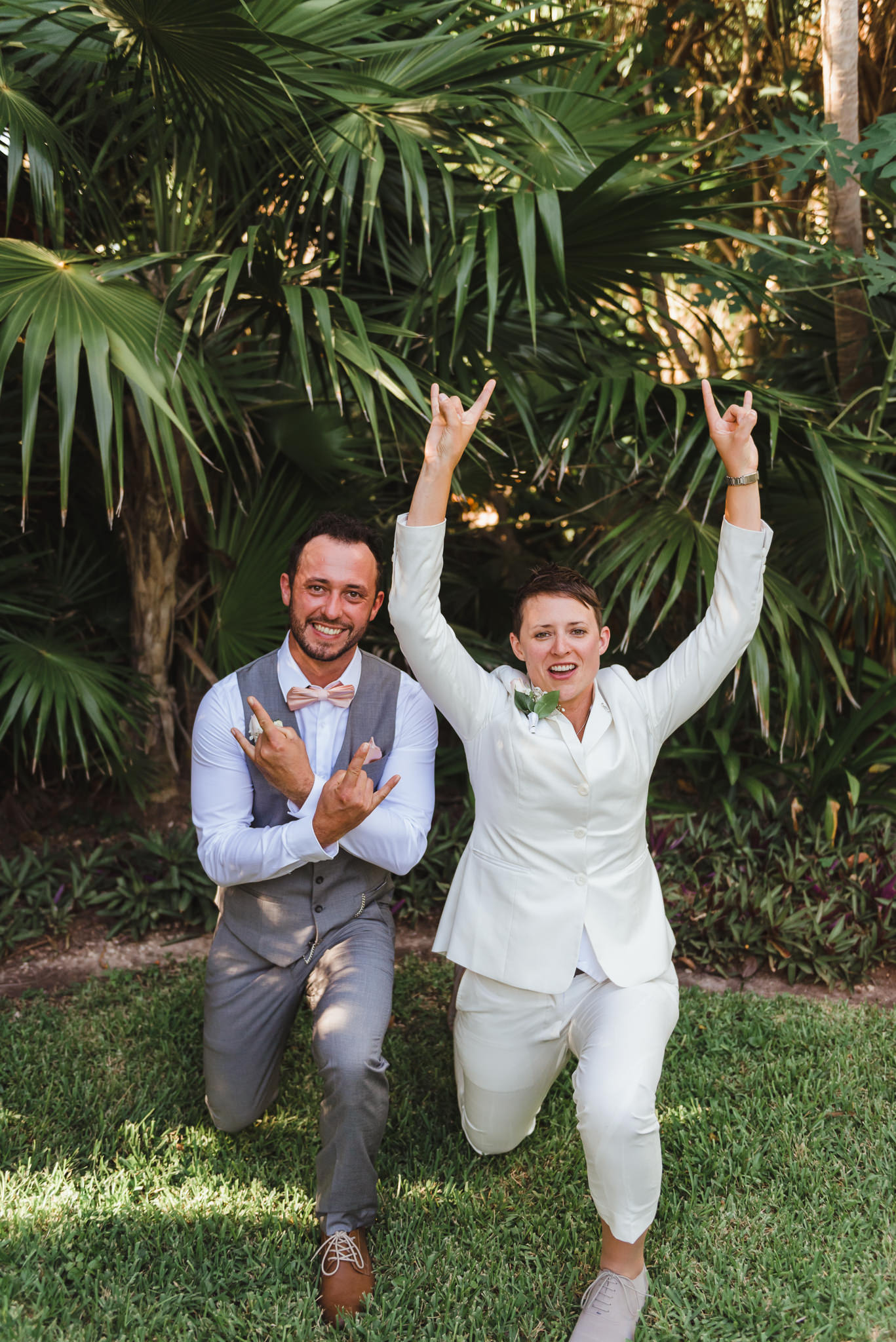 bride and wedding guest crouched down on grass doing rock on symbol with their hands Now Sapphire Resort beach ceremony Mexico