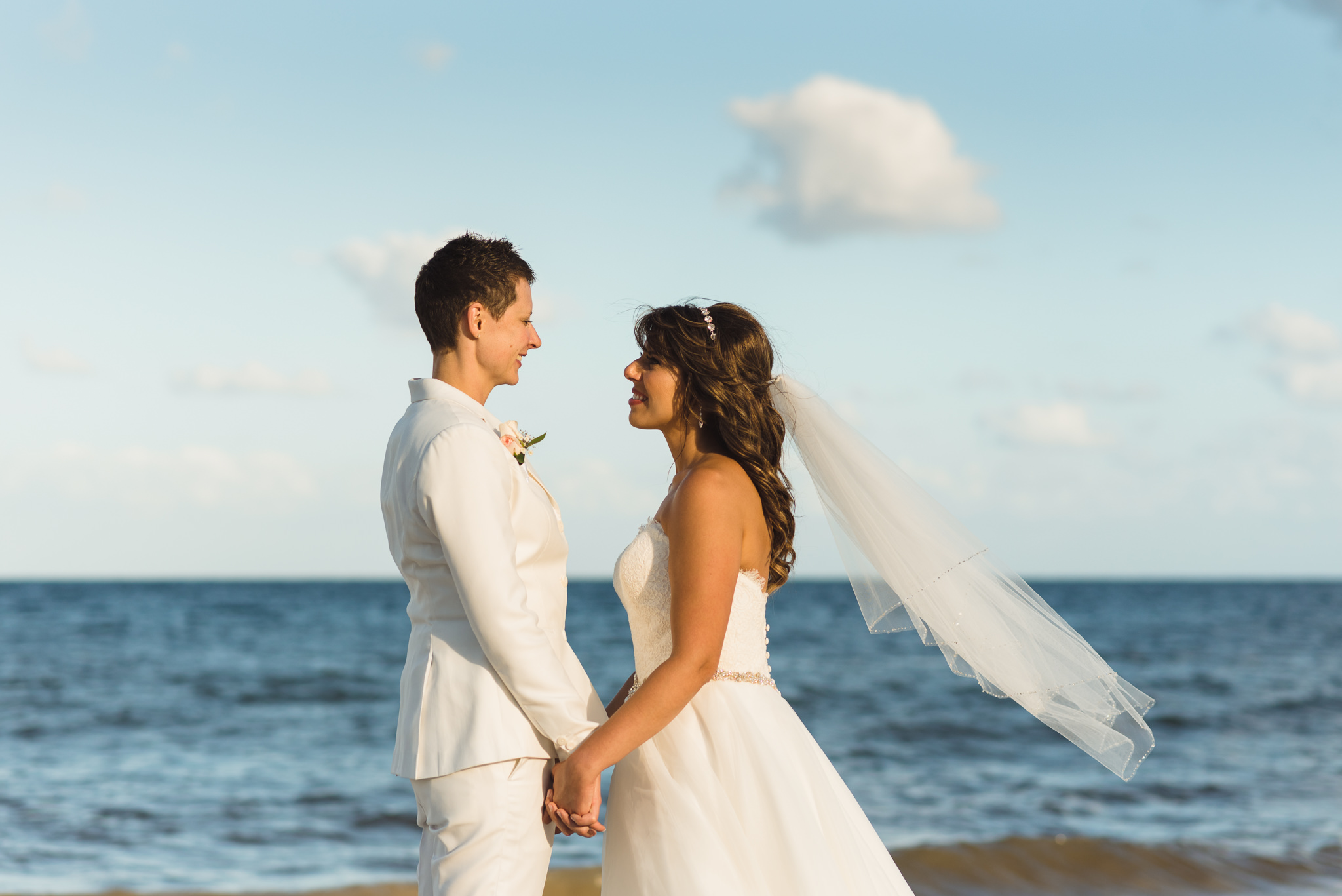 brides facing each other and holding hands in front of the ocean after beach ceremony at Now Sapphire Resort in Mexico