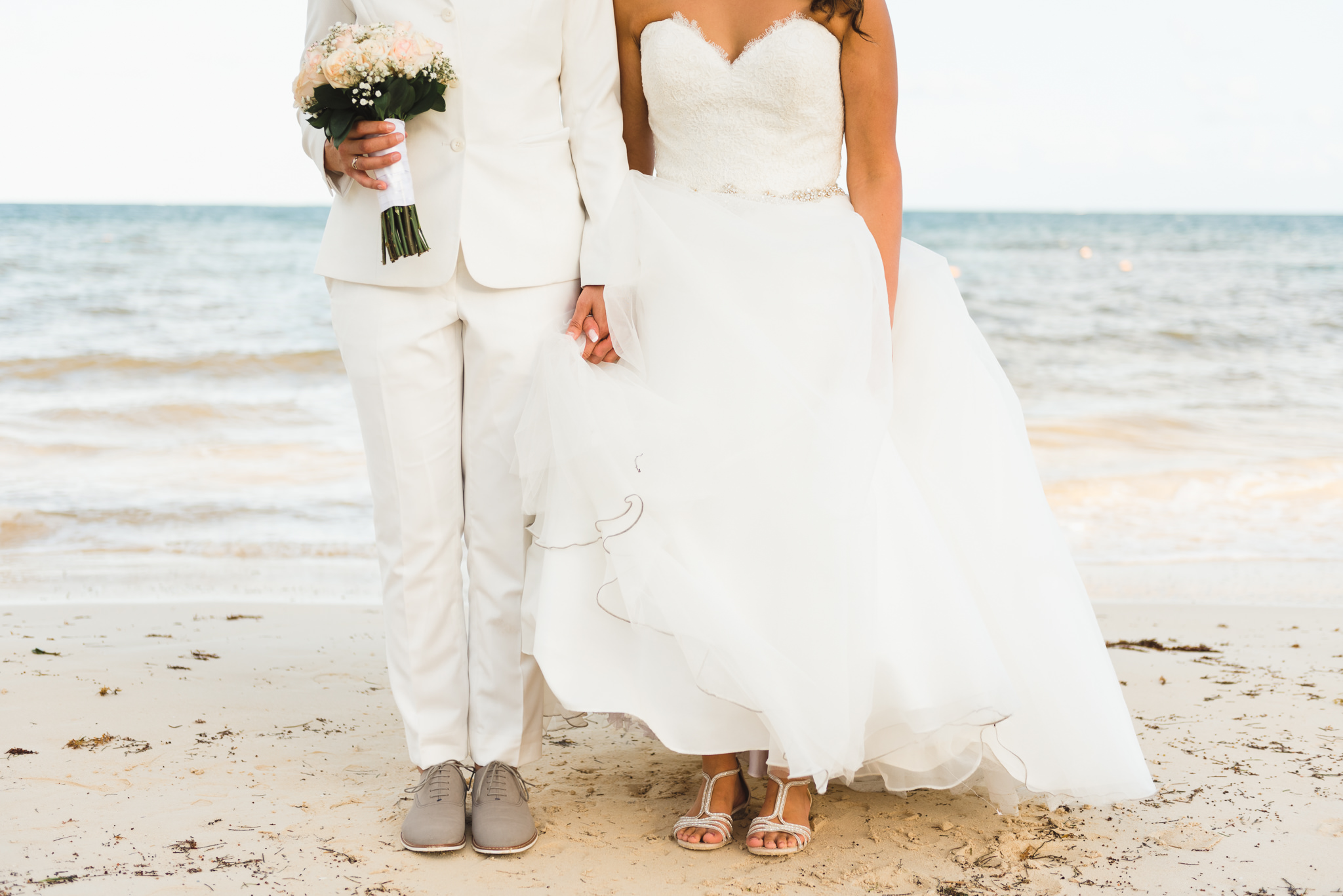 brides standing side by side on the beach holding hands and bouquet after ceremony at Now Sapphire Resort in Mexico