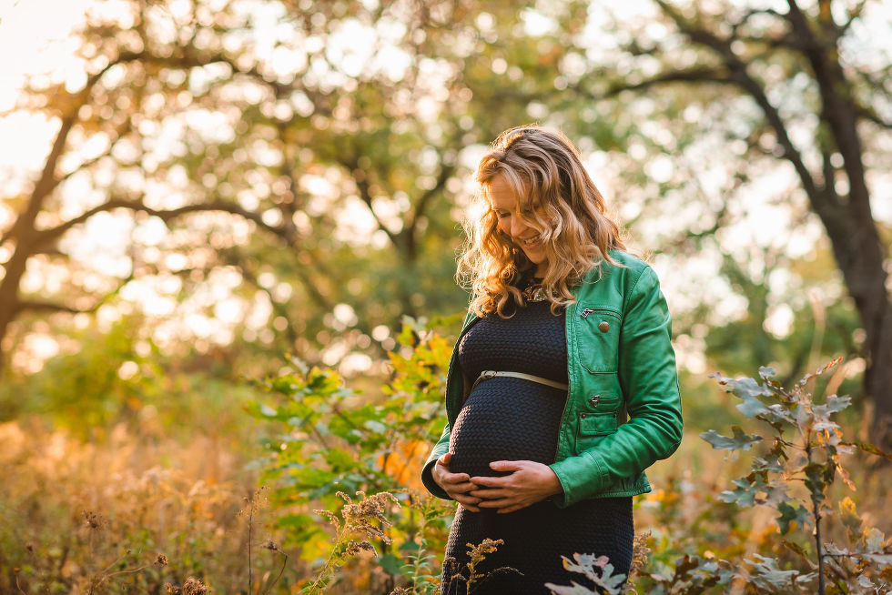 woman holding her pregnant belly while standing amongst the autumn foliage of High Park, Toronto