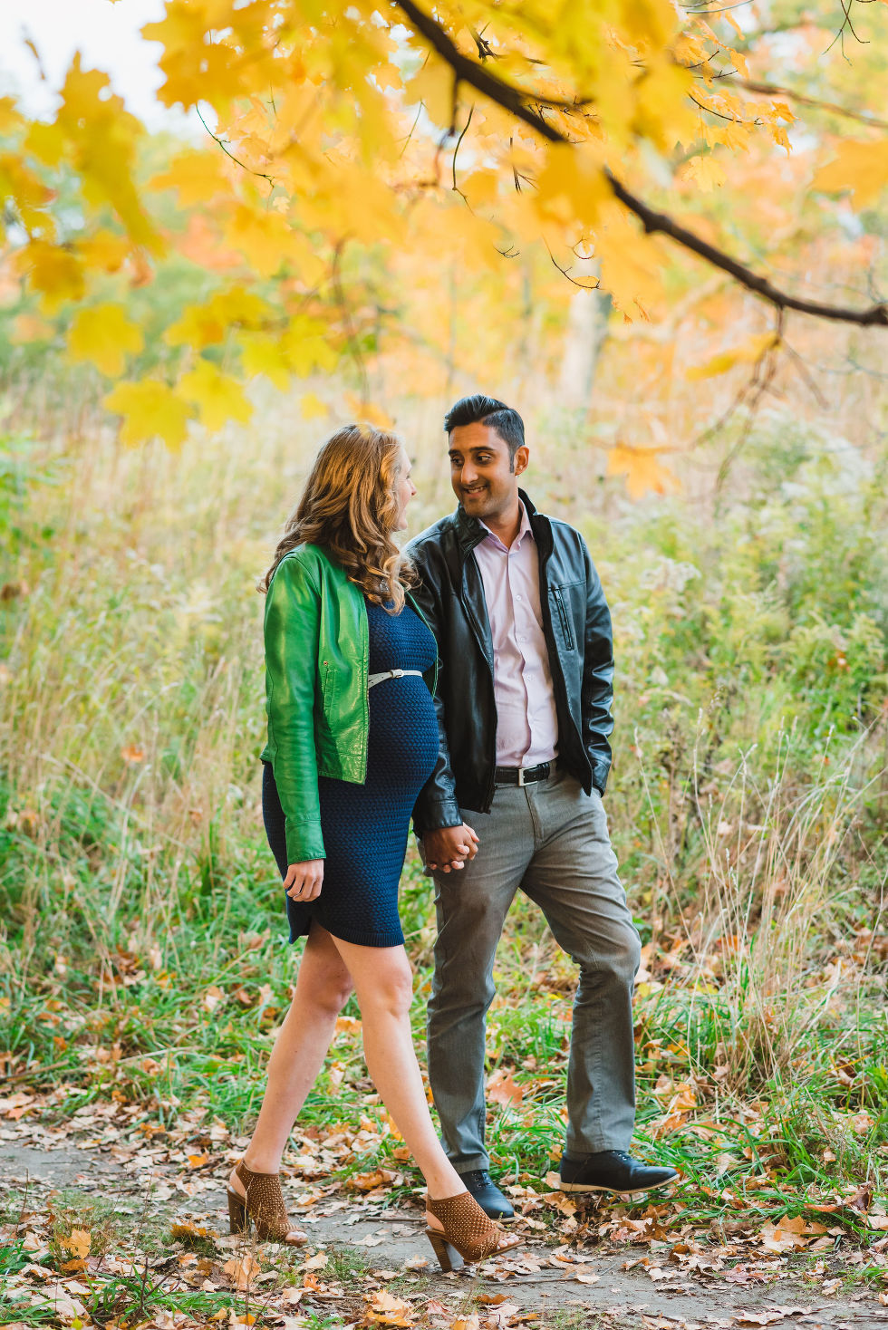 Pregnant couple walking beneath autumn foliage in High Park, Toronto