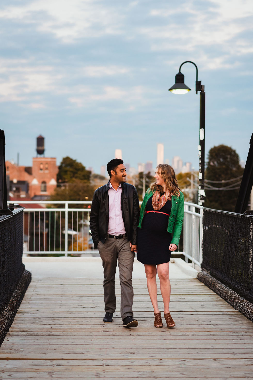 man and woman stroll together holding hands on train platform in the Junction with Toronto skyline in background