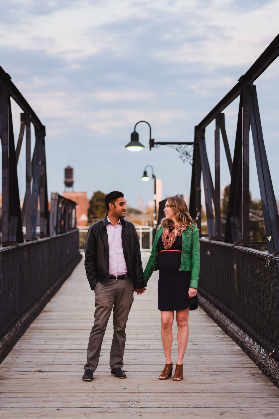 man and woman stroll together holding hands on a bridge in the Junction with Toronto skyline in background