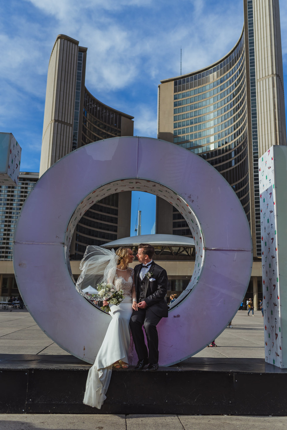 married couple sitting in the letter "O" in Toronto sign at Nathan Phillips Square how to plan an amazing iconic downtown Toronto wedding