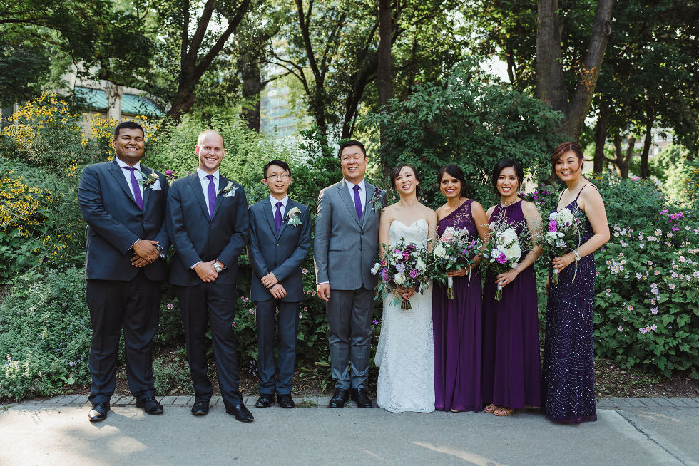 bride and groom stand in between their wedding party in the park before their Parisian inspired wedding at La Maquette in Toronto Ontario