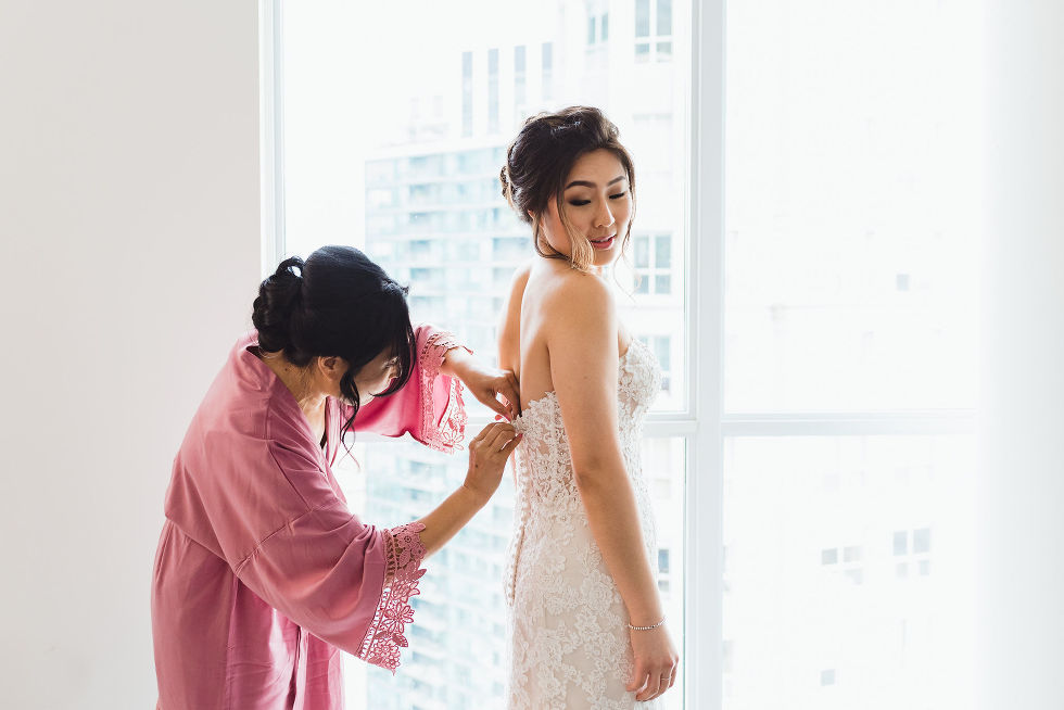 bridesmaid helping bride do up the back of her wedding dress before her wedding at Fantasy Farms in Toronto Ontario