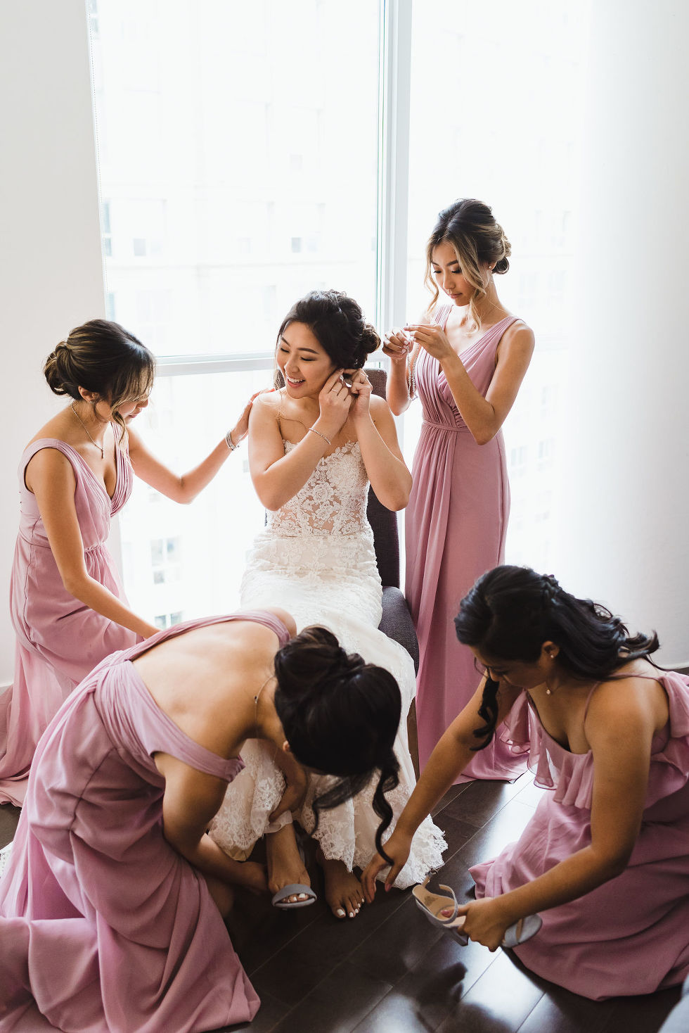 bride sitting down putting on her earrings while her bridesmaids help her get ready for her wedding at Fantasy Farms in Toronto Ontario