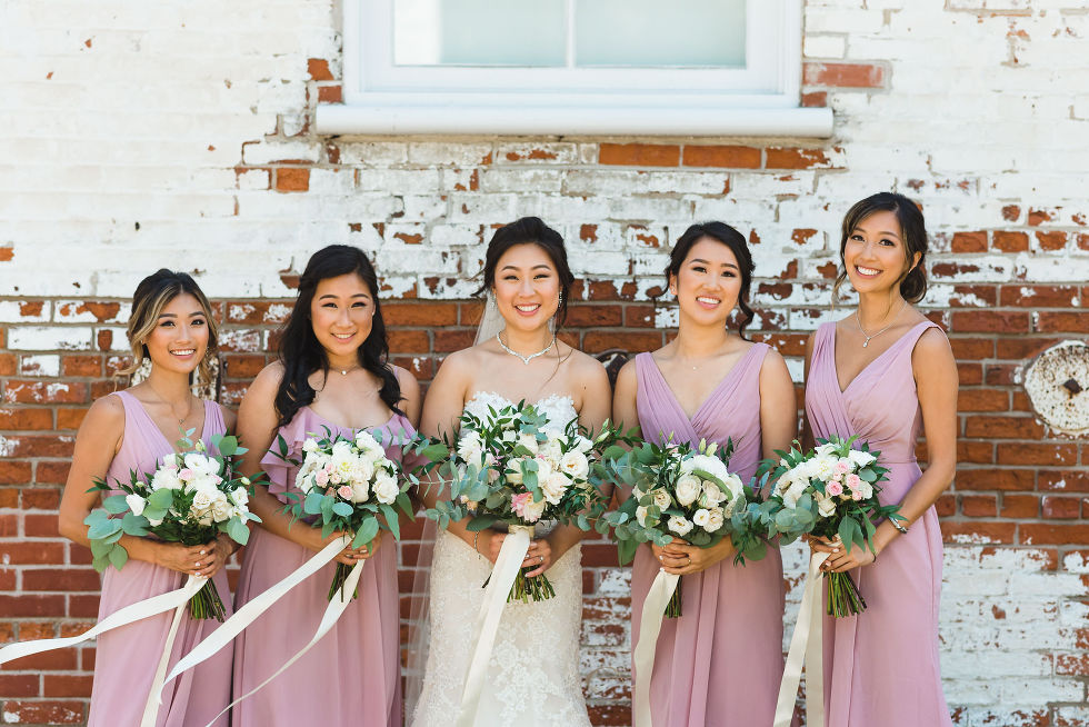 bride and bridesmaid in lavender coloured dresses standing in front of red and white brick wall on wedding day atFantasy Farms in Toronto Ontario