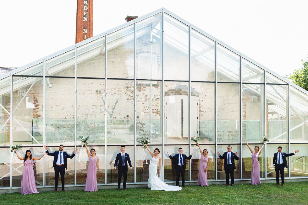 bridal party holding up bouquets and arms standing in front of glass brick building at Fantasy Farms in Toronto Ontario