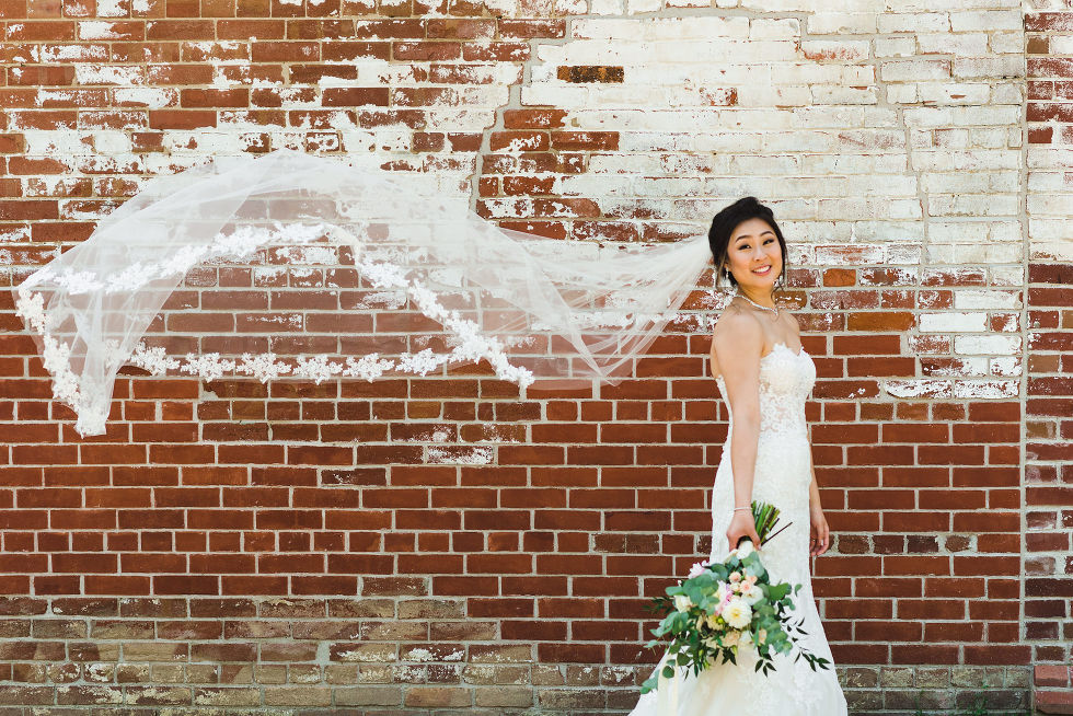brides veil waving up in the air in front of old vintage brick wall on her wedding day at Fantasy Farms in Toronto Ontario