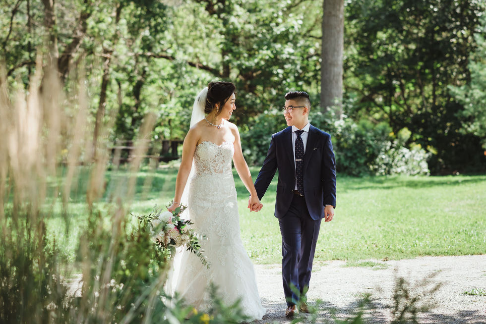 bride and groom walking through greenery garden holding hands at Fantasy Farms in Toronto Ontario