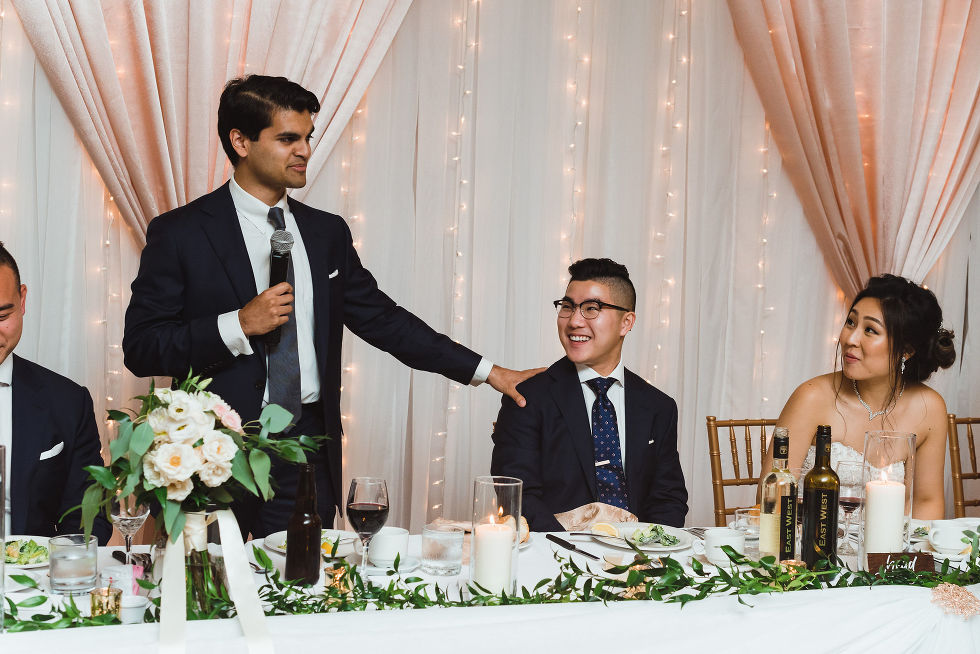 best man putting hand on shoulder of groom holding a microphone giving a speech at wedding at Fantasy Farms in Toronto Ontario