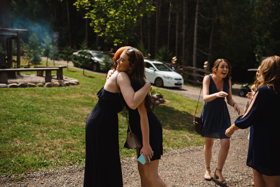 A group of women smiling and hugging as they arrive in a cottage driveway Toronto wedding photography