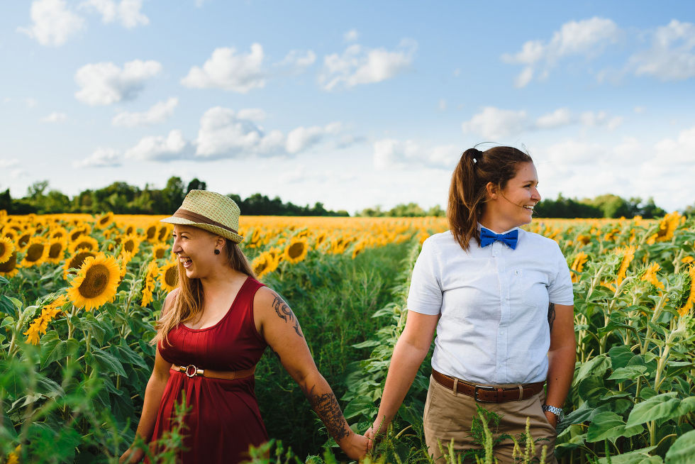 2 women holding hands and smiling while standing in a stunning sunflowers field Toronto engagement photos
