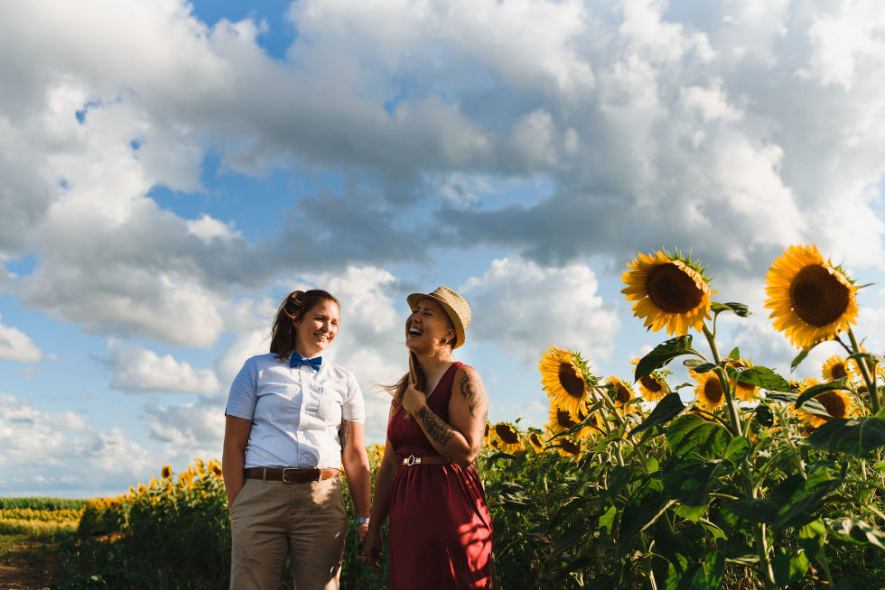 2 women smiling and holding hands on the edge of a stunning sunflower field Toronto engagement photography