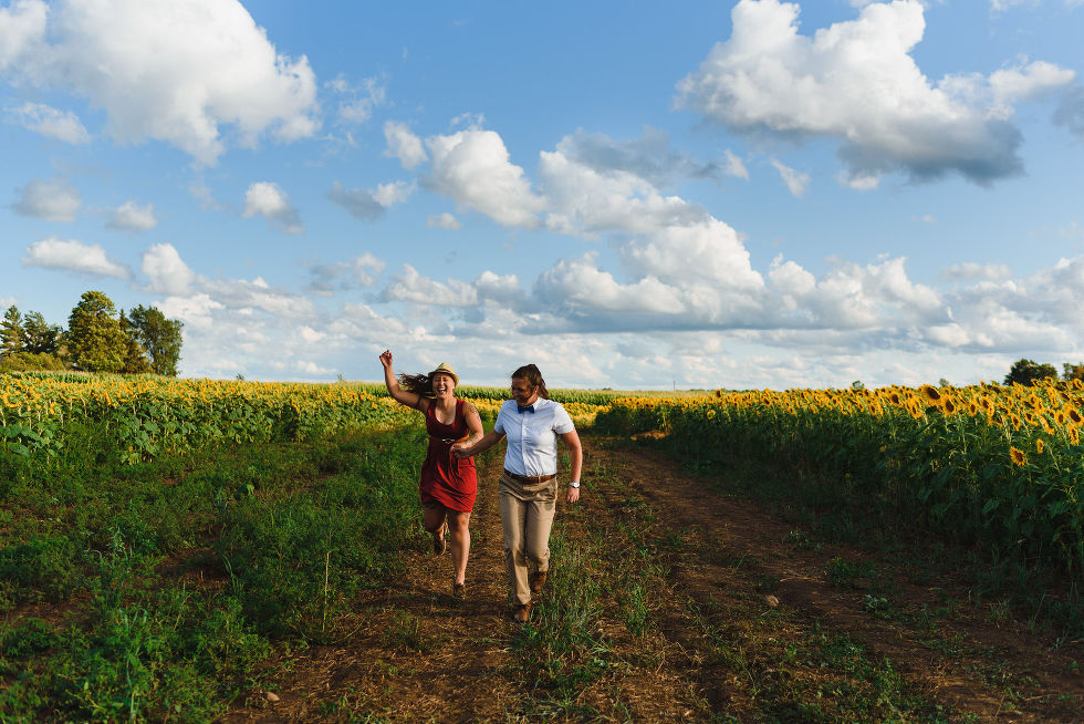 2 women running hand in hand next to a stunning sunflower field for their engagement photoshoot