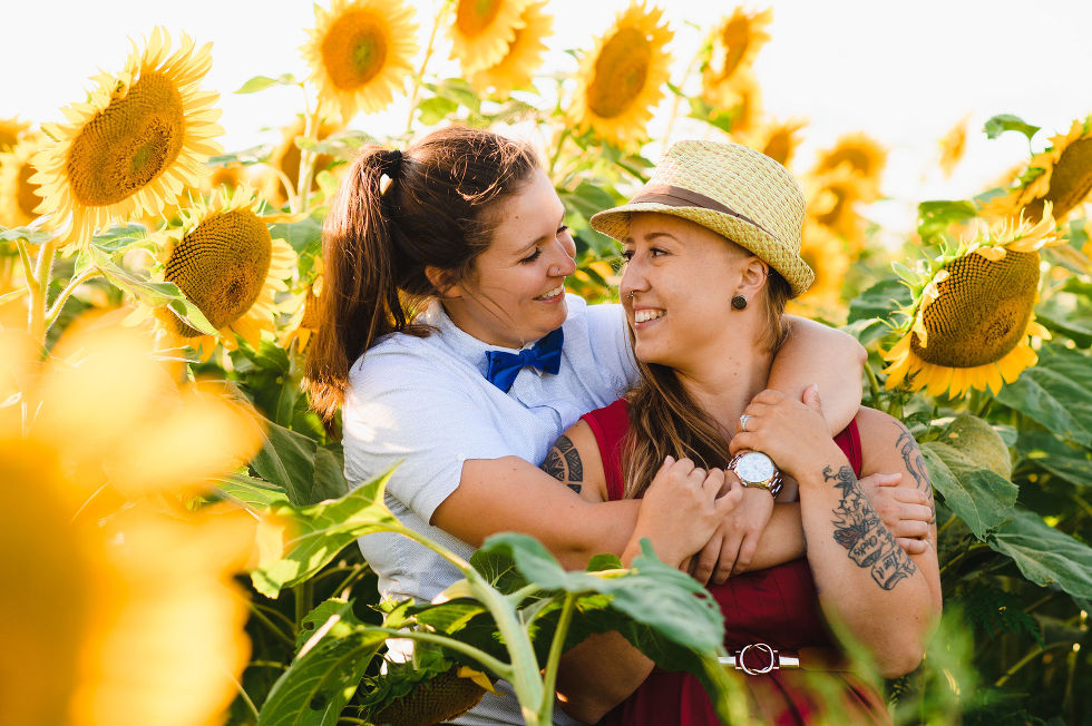engaged couple with arms wrapped in a loving embrace standing amongst a stunning sunflower field Toronto engagement photos