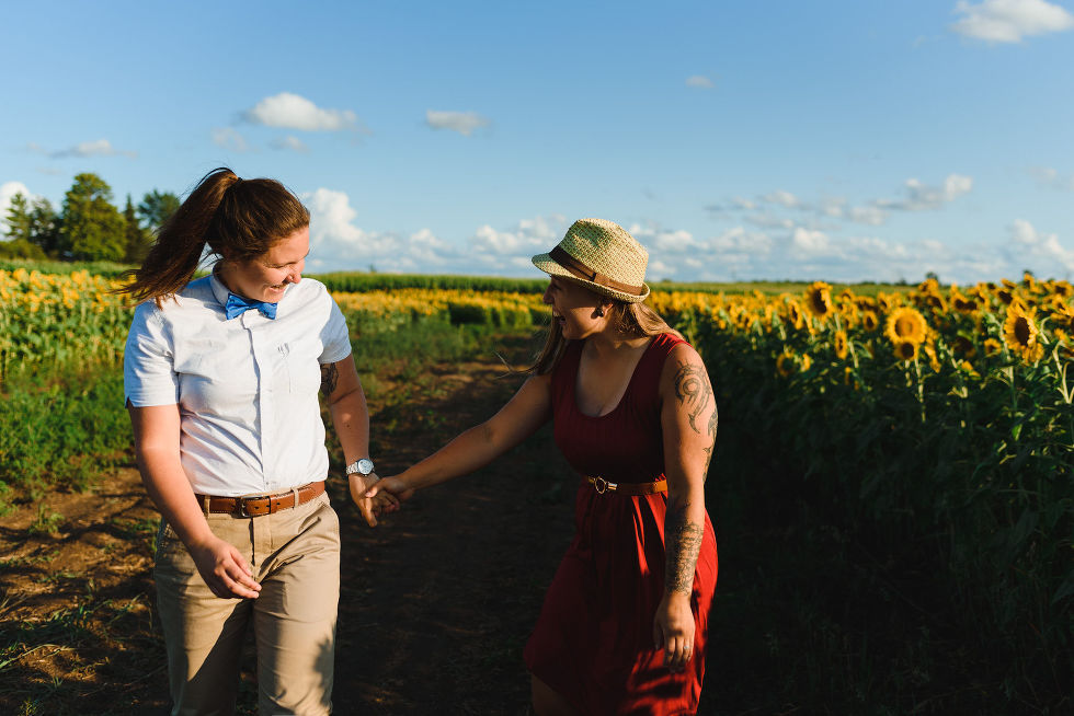 engaged couple laughing and holding hands as they exit a stunning sunflower field during their engagement shoot
