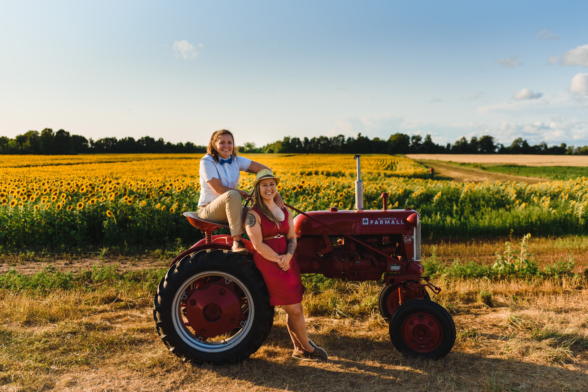 engaged couple sitting side by side on a tractor in front of a stunning sunflower field Toronto engagement photography