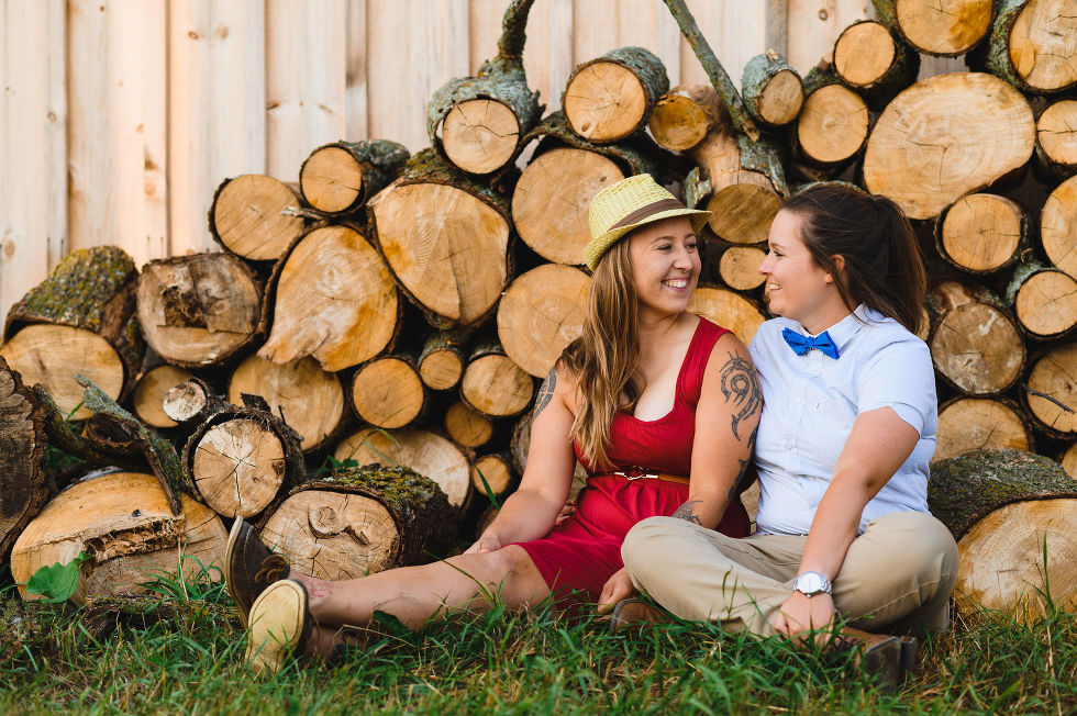 engaged couple sitting side by side in front of a barn and a stack of firewood at their backs Toronto engagement photos
