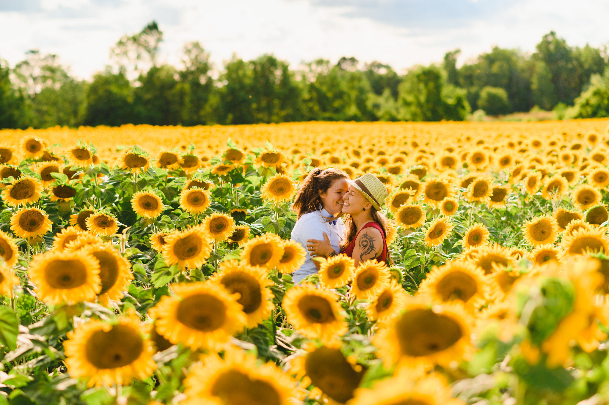 2 women with their arms wrapped around each other and laughing while standing in stunning sea of sunflowers Toronto engagement photos