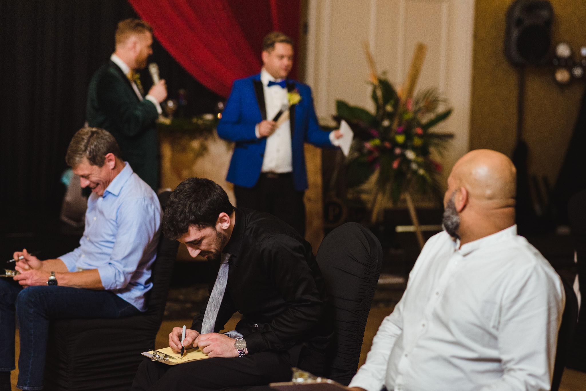 grooms reading game instructions into their microphones while seated guests are scribbling away on clipboards during a fun wedding at the Hilton Fallsview in Niagara Falls