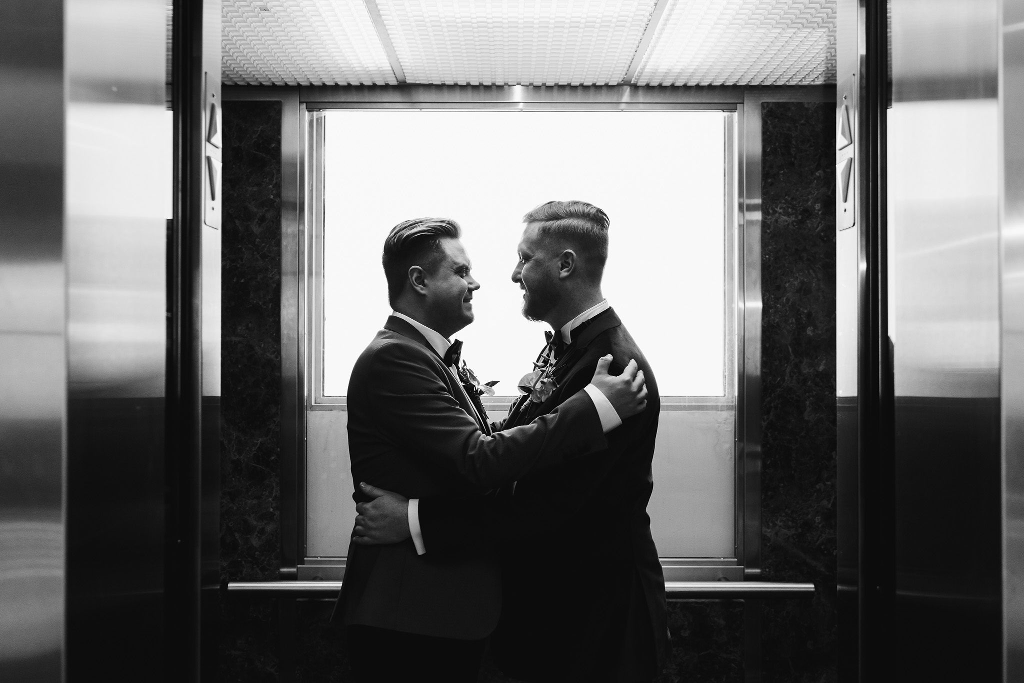 grooms with their arms wrapped in a loving embrace in an elevator at the Hilton hotel in Niagara Falls wedding photography