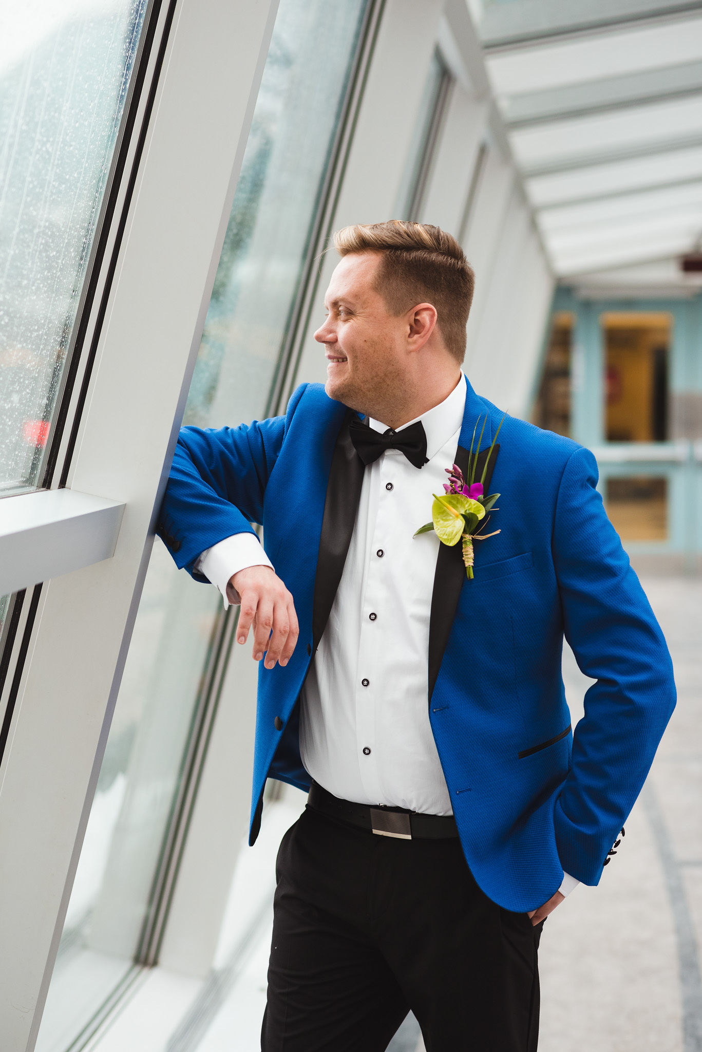 groom in bright blue suit stares out the window before his wedding ceremony at the Hilton Fallsview in Niagara Falls