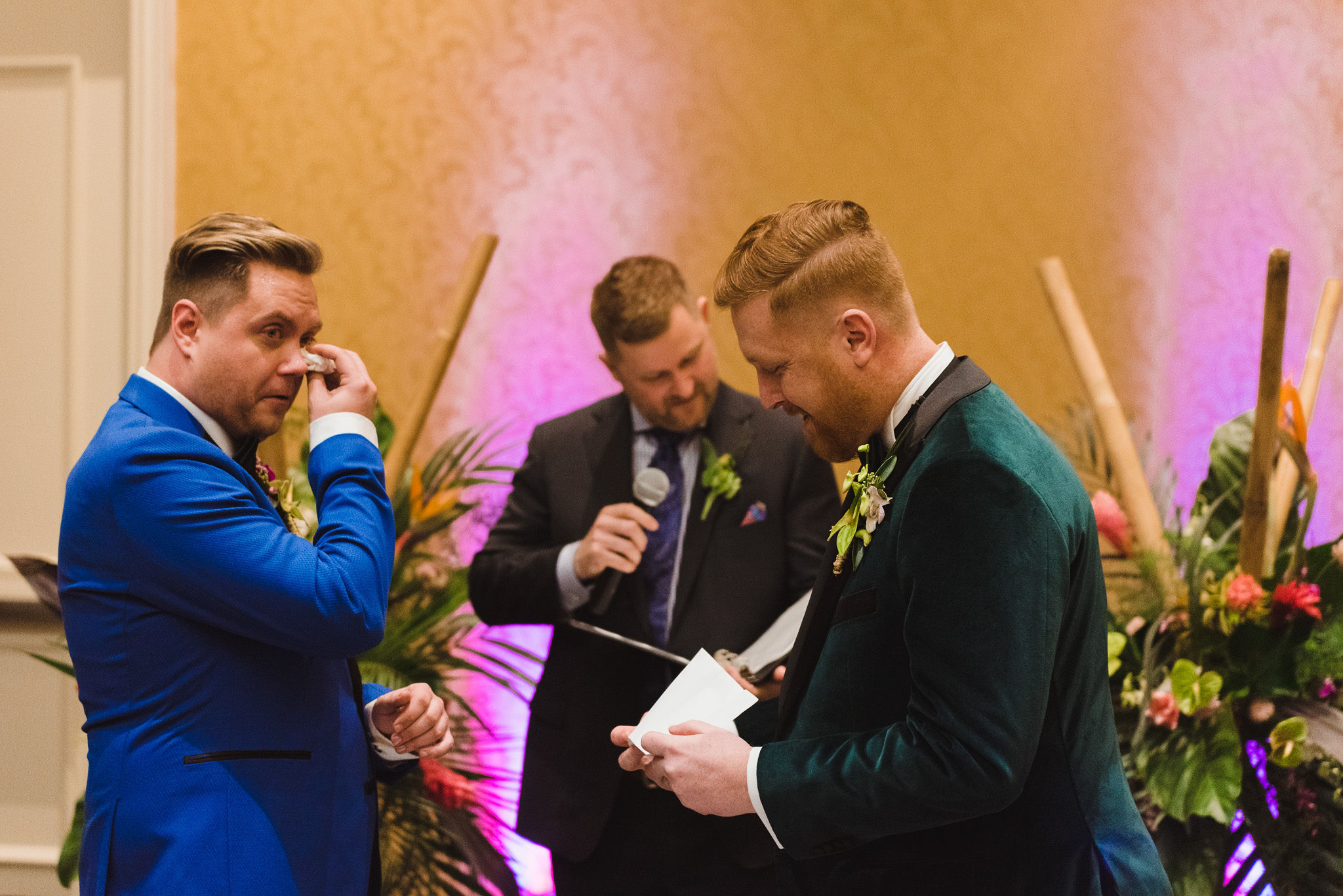 groom in bright blue suit wiping tears from his eyes while his groom reads vows during wedding ceremony at the Hilton Fallsview in Niagara Falls