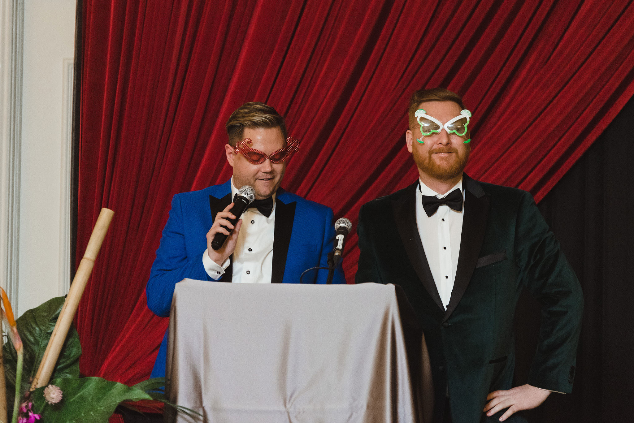 grooms wearing wacky glasses as they read speeches at the podium during their wedding reception at the Hilton Fallsview in Niagara Falls
