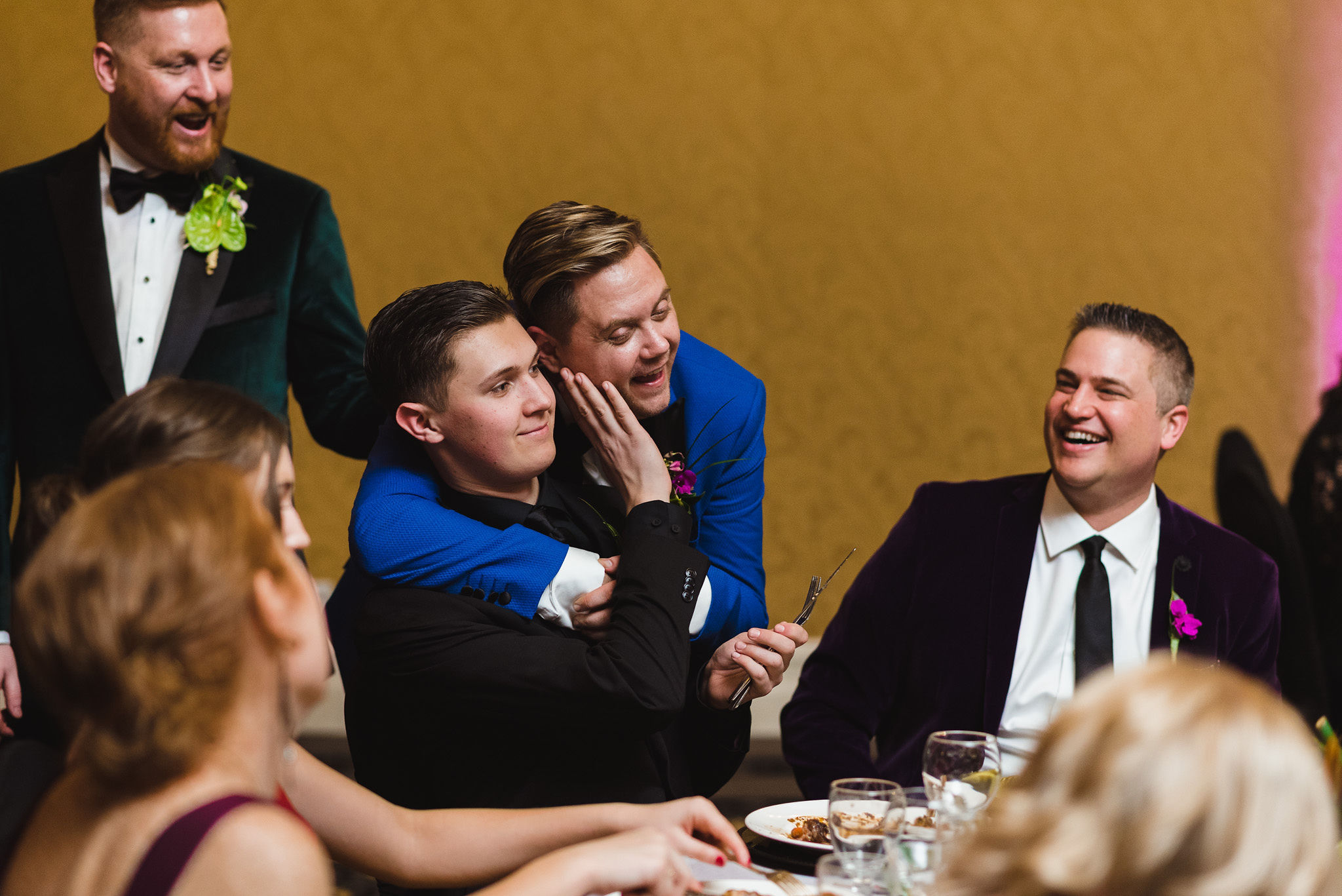 groom wrapping his arms around a wedding guest seated at a table with the other guests laughing during the reception at the Hilton Fallsview in Niagara Falls
