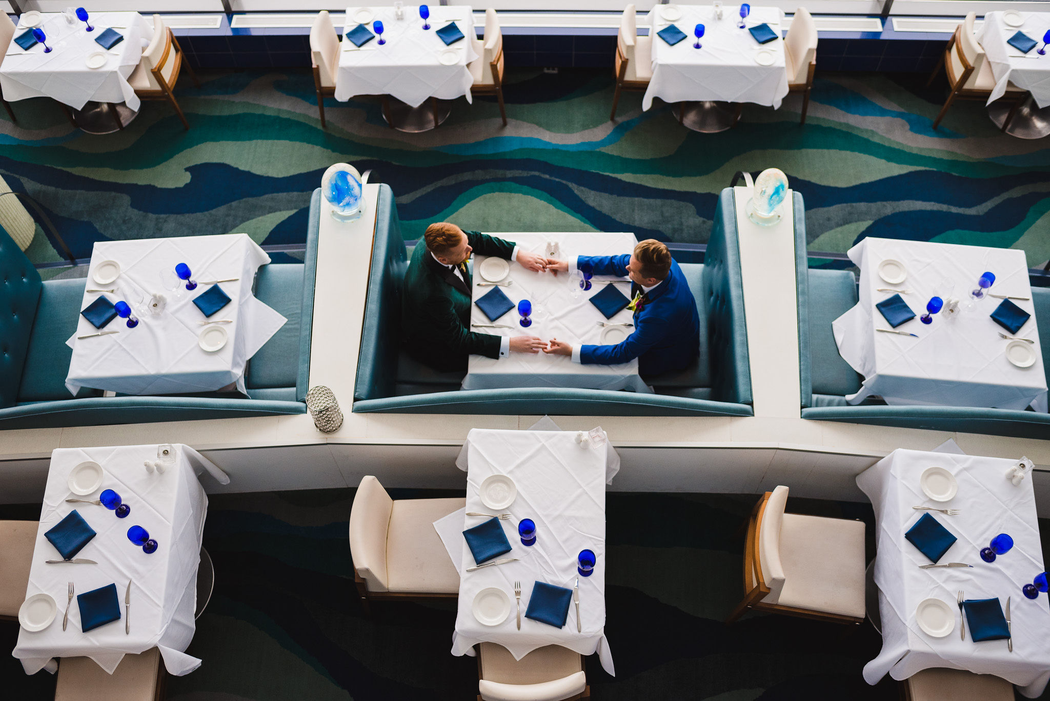 aerial shot of grooms holding hands across the table while sitting in a booth in the Hilton hotel in Niagara Falls before their wedding ceremony