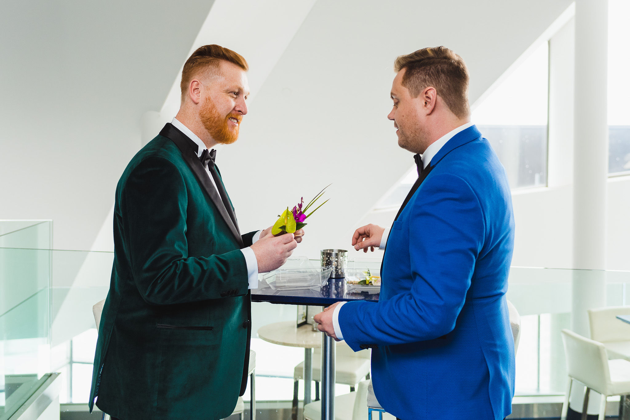 groom in a green suit holding boutonniere in front of groom in bright blue suit before wedding ceremony at the Hilton in Niagara Falls 