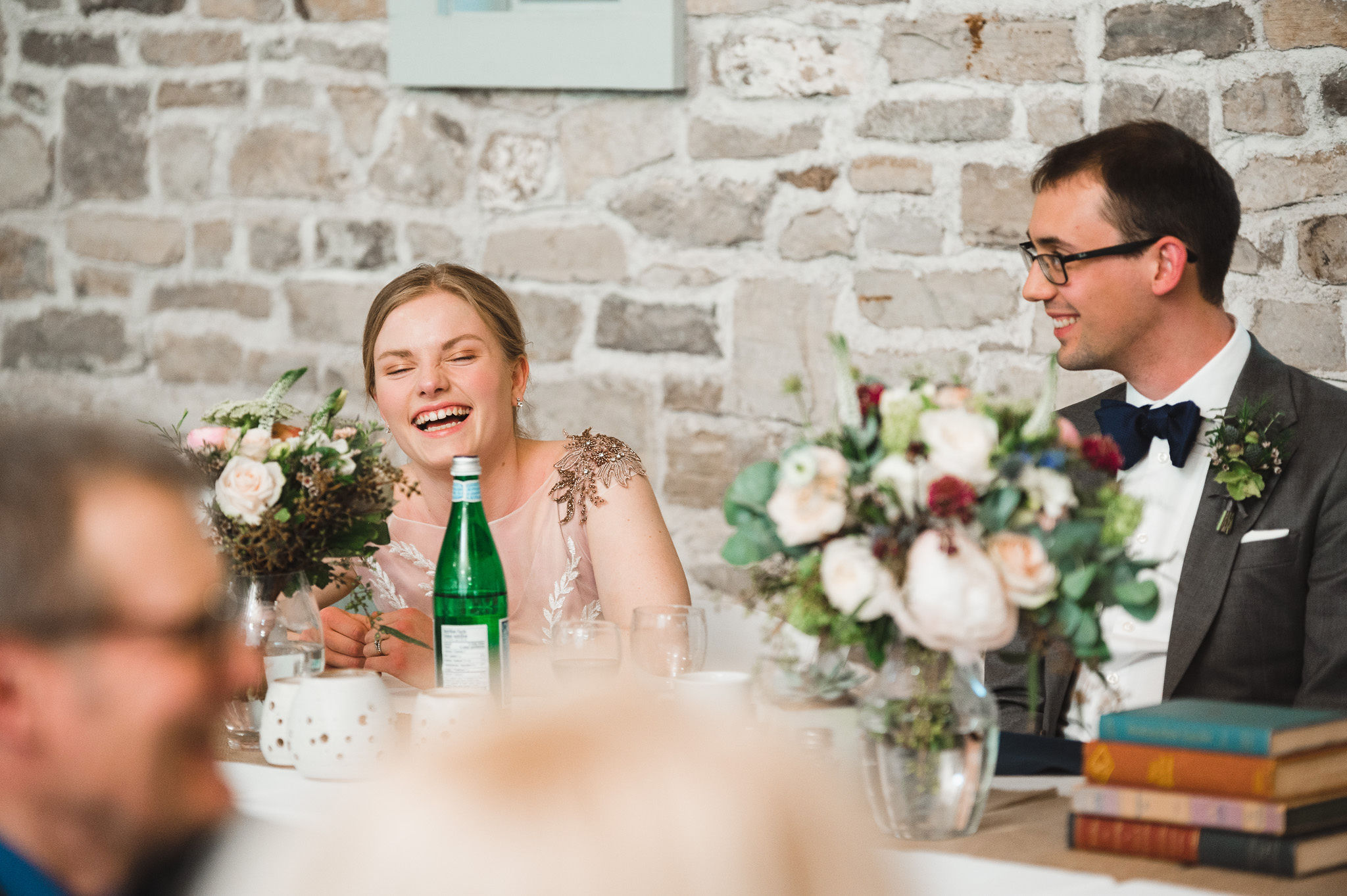 bride and groom laughing at their head table in front of an old stone wall during their charming southern style wedding at Ruthven National Historic Site near Hamilton
