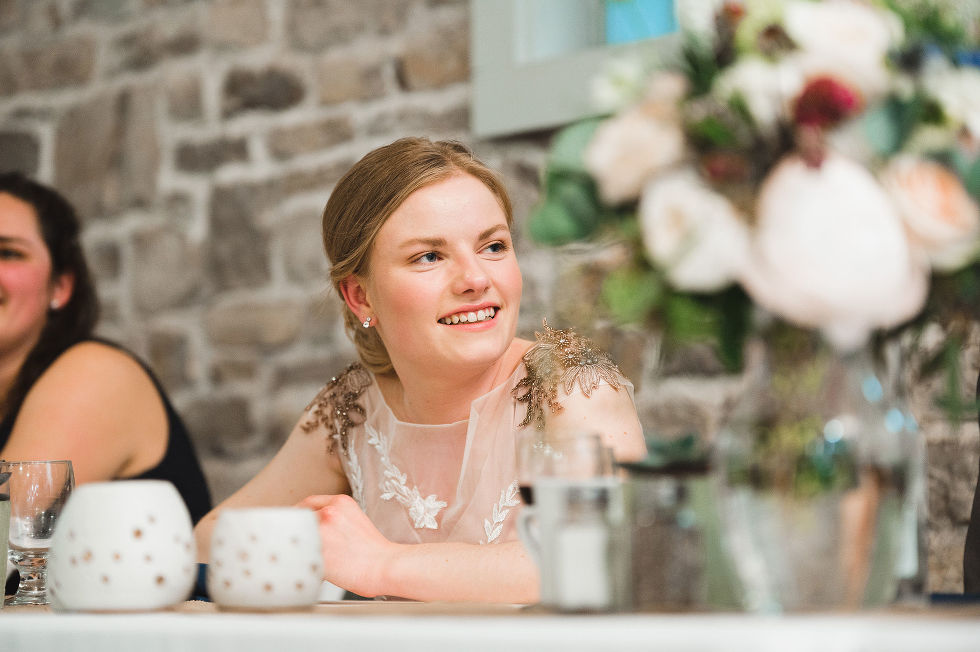 bride smiling while sitting at the head table in front of old stone wall during speeches for her wedding at Ruthven National Historic Site