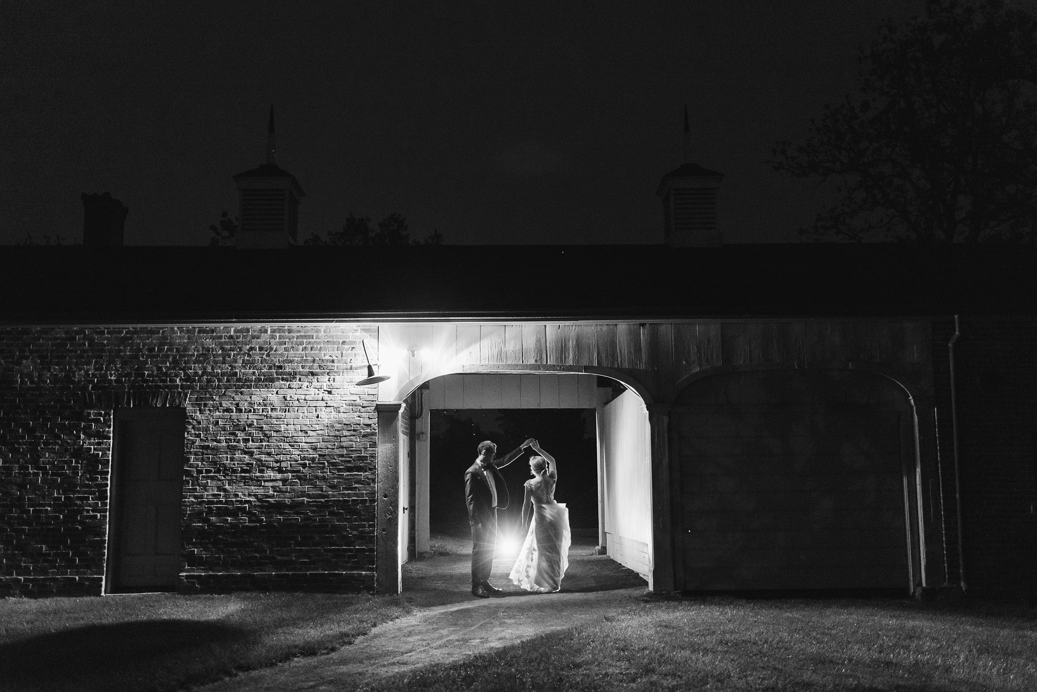 groom twirling his bride at dusk between an old stone building after their charming southern style wedding at Ruthven National Historic Site