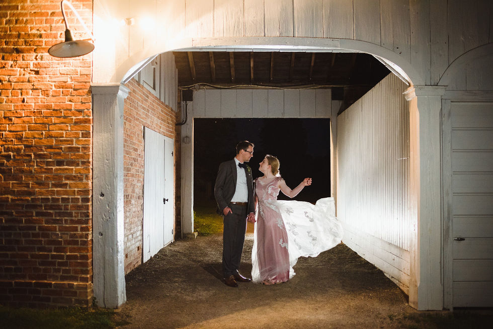 bride and groom standing together in a loving embrace at dusk between an old stone building after their charming southern style wedding at Ruthven National Historic Site