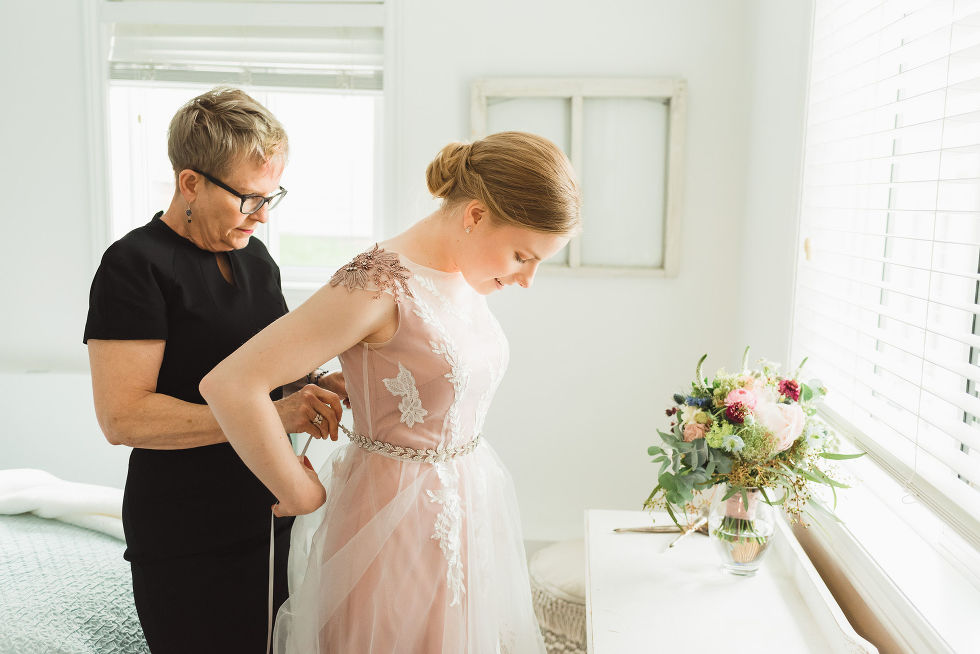 mother of the bride helping her daughter do up her wedding dress before her charming southern style wedding at Ruthven Park National Historic Site