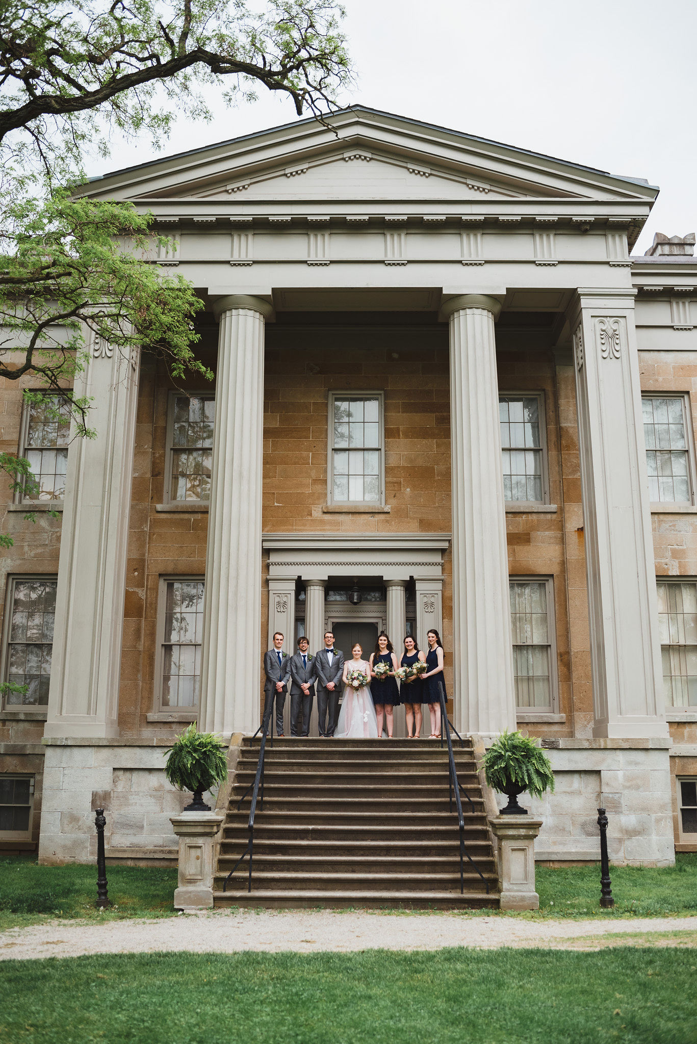 bride and groom standing between their wedding party on stone steps between Greek stone columns of the Ruthven National Historic Site near Hamilton