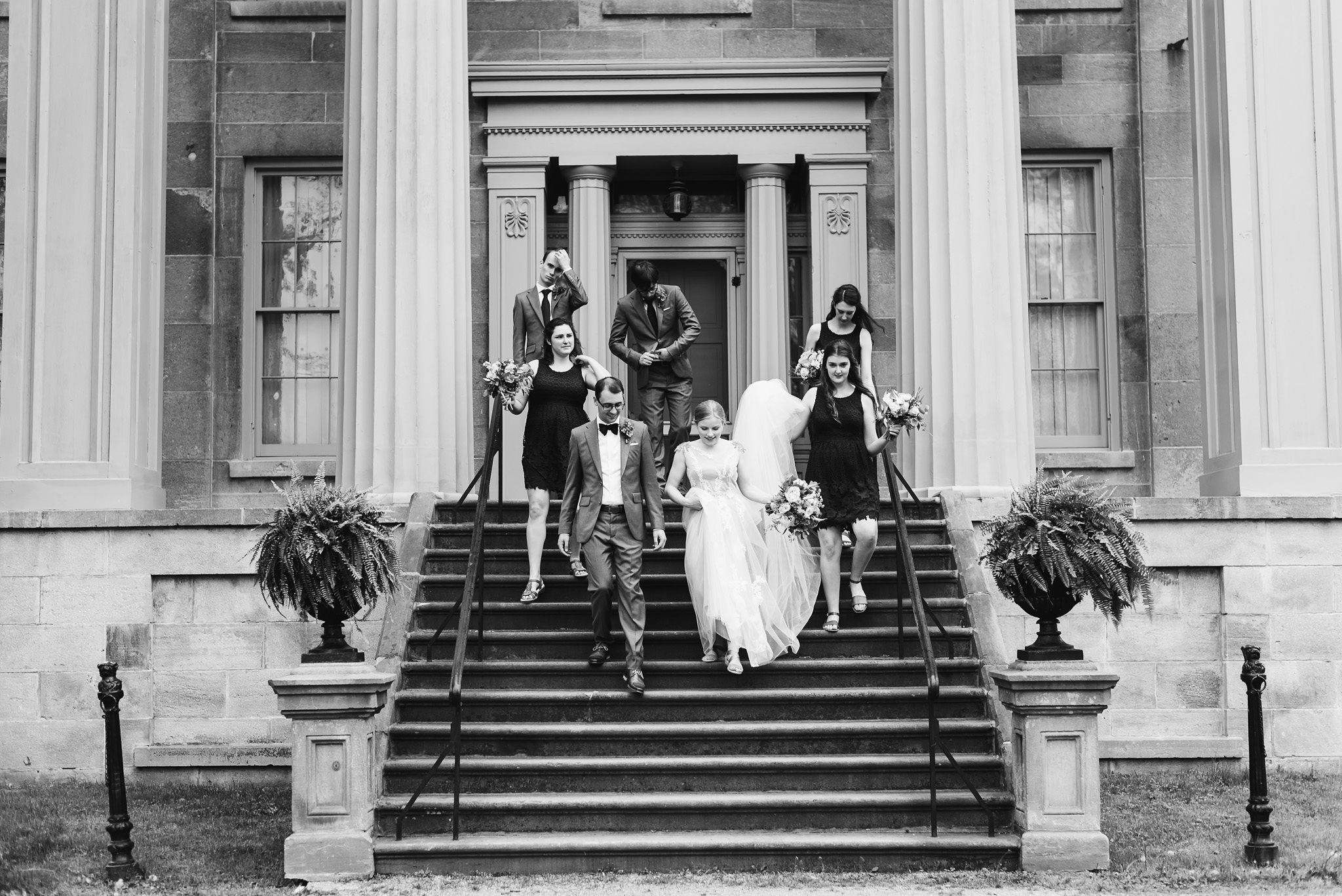 bride and groom walking down the steps with their wedding party between Greek stone columns of the Ruthven National Historic Site after their charming southern style wedding near Hamilton