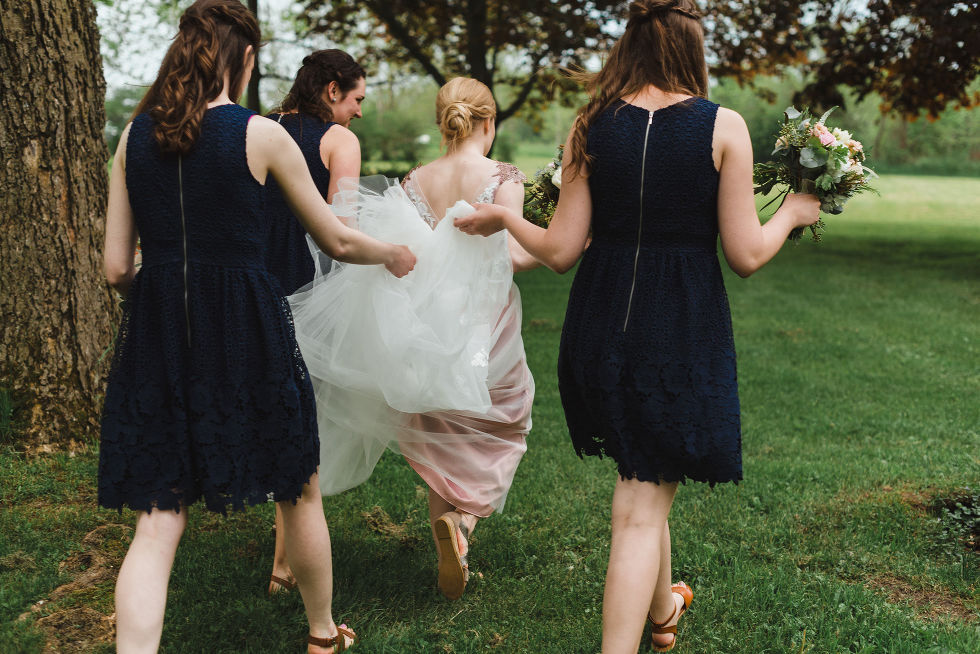 bride strolling on the lawn of the Ruthven National Historic Site while her three bridesmaids hold the back of the dress during her charming southern style wedding near Hamilton
