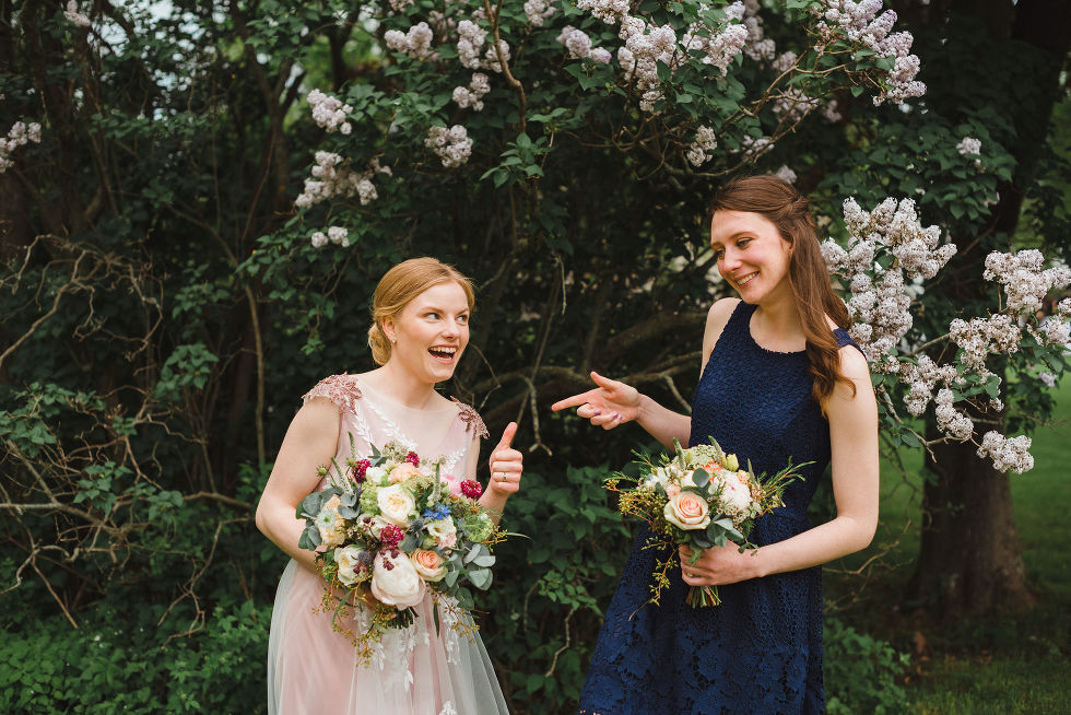 bride holding a floral bouquet and giving a thumbs up to her bridesmaid that is holding out her hand in the shape of a gun during her charming southern style wedding at Ruthven National Historic Site