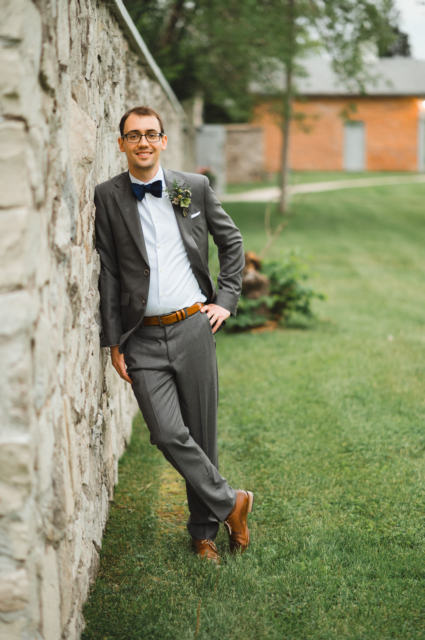 groom smiling and leaning against old stone wall during his charming southern style wedding at Ruthven National Historic Site near Hamilton