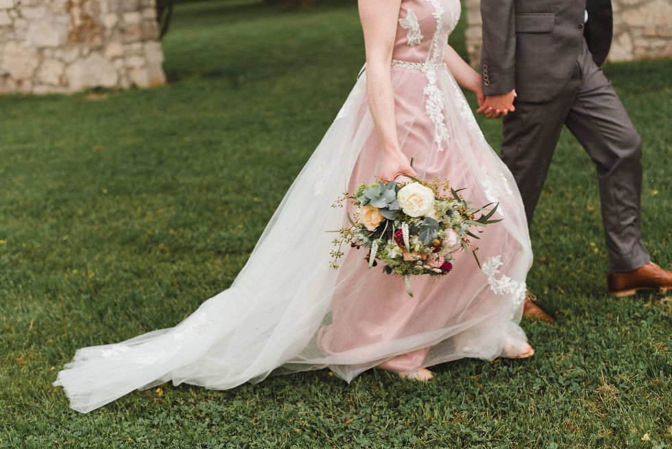 bride holding colourful bouquet of flowers as she and her groom stroll hand in hand across the lawns of the Ruthven National Historic Site during their harming southern style wedding